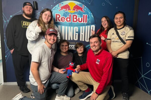 Shenandoah University esports students and staff gathered around a logo (backdrop) for PXL Esports’ Red Bull Gaming Hub in Belgium.