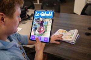 A person holds a tablet demonstrating the "Lo and Behold" augmented reality companion app.