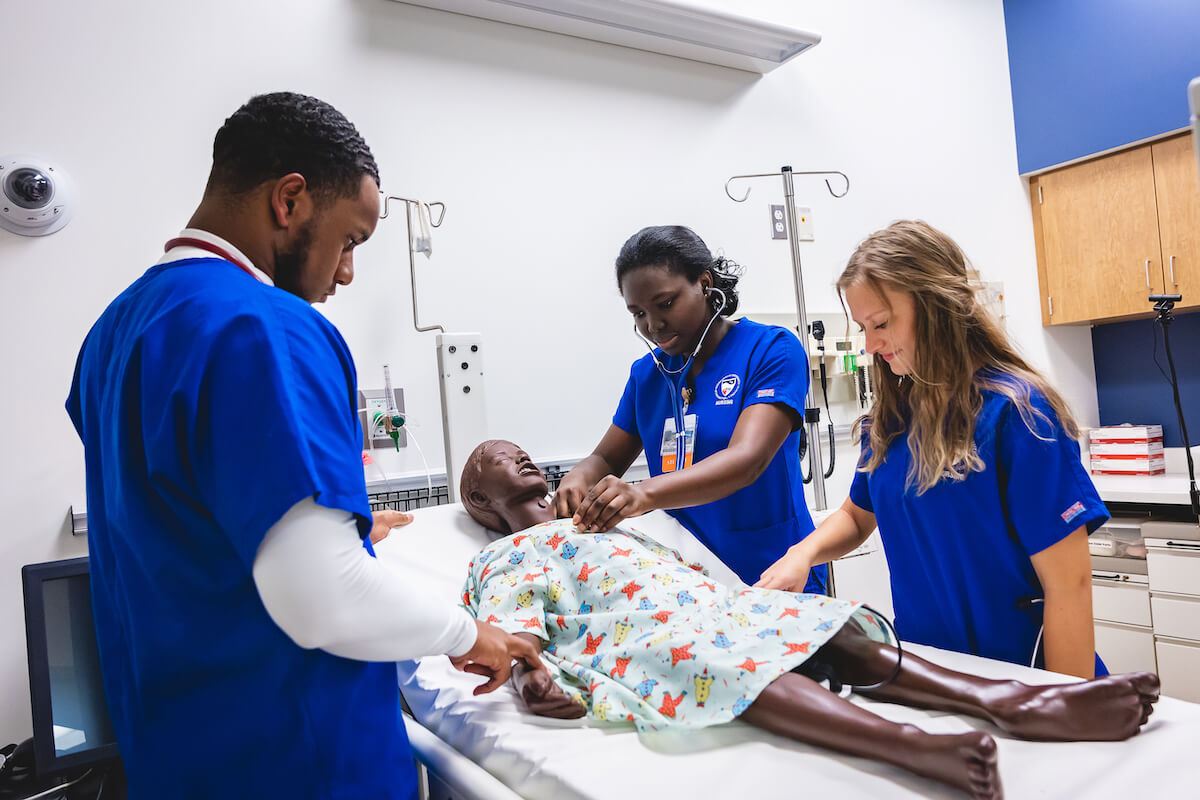 Three Shenandoah University nursing students simulating care by working with a manikin.