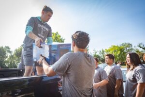 Shenandoah University football players unload a microwave from a pickup truck.