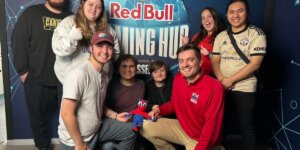 Shenandoah University esports students and staff gathered around a logo (backdrop) for PXL Esports’ Red Bull Gaming Hub in Belgium.